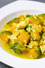 Fried pumpkin with egg for children in white dish on concrete table.