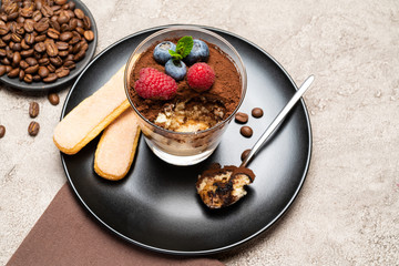 Classic tiramisu dessert portion with blueberries and raspberries in a glass cup on concrete background