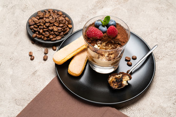 Classic tiramisu dessert portion with blueberries and raspberries in a glass cup on concrete background