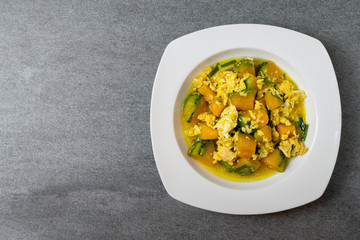 Fried pumpkin with egg for children in white dish on concrete table.