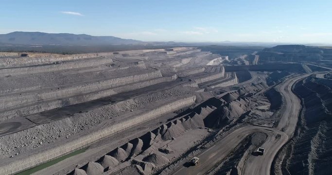 Black coal open cut mine in Hunter Valley moved by huge industrial trucks from the bottom up to the surface in aerial top down view.