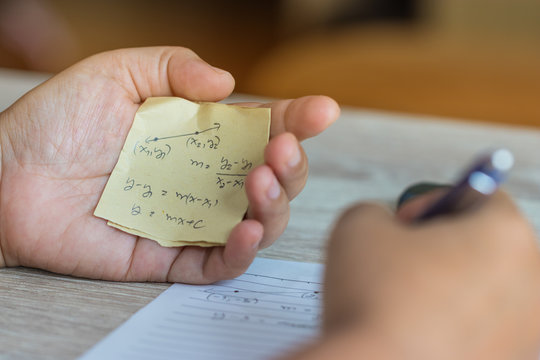 Student using formula math sheet to cheat on test. Hand of university student holding pencil doing math question in examination and cheating with answer piece of paper in hand. Education concept.