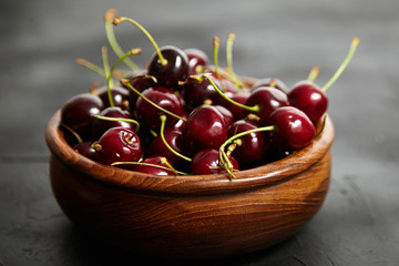 Ripe cherries in a wooden bowl on a black stone table. Red  berries on a dark background