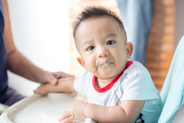 Fototapeta premium Asian baby child boy sitting on baby chair try to eating blend food