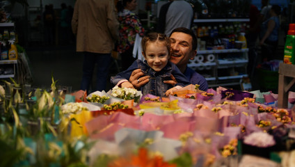 Portrait of cute little girl choosing flowers in supermarket with happy dad