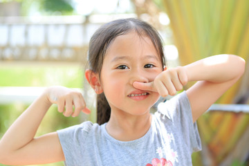 Attractive smiling little child girl touching nose with thumb with expression happy and relax outdoor. Portrait Asian kid in garden.