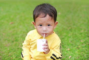 Portrait of little baby boy in sport cloth drinking milk from box with straw in the garden.