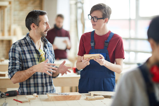 Waist up portrait of mature carpenter talking to young trainee in workshop, copy space