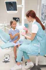 Child dentist wearing uniform teaching girl to brush teeth