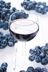 glass of red wine and blue grapes on white wooden table background