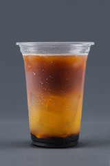 Cold drink with coffee, orange juice and ice cubes on a gray background