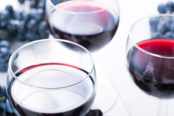 three glasses of red wine and blue grapes on white wooden table background