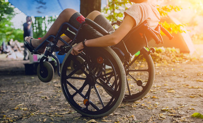 Disabled man resting in a campsite with friends. Wheelchair in the forest on the background of tents