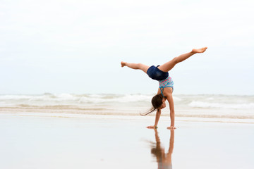 Obraz premium Sport, training, fitness, yoga, active lifestyle concept. Flexible girl gymnast doing acrobatic exercise at the beach.