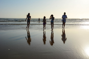 Mother with son and daughters running into the ocean before sunset. 