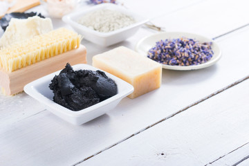 spa products: black mud and clay powder, cosmetic cream, soap, bath salt, shea butter and lavenders on white wood table background