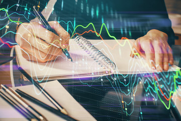 Forex chart hologram on hand taking notes background. Concept of analysis. Multi exposure