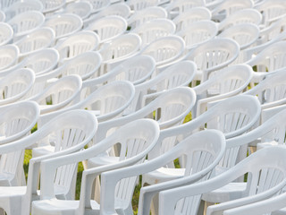 Group of white plastic armchairs on green grass field with shadows in sunny day.