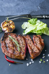 The cutted ribeye steak with sprig of rosemary on a black stone slab