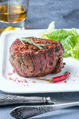 Chateaubriand on a white plate with green lettuce and a glass of whiskey in the background