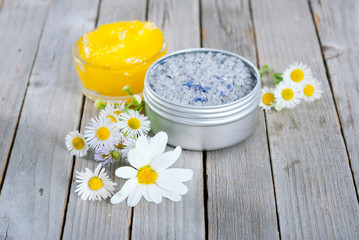 Obraz na płótnie Canvas yellow calendula cream in glass pot, moisturizer and bath salt with white herbal flowers on weathered rusty wooden table background
