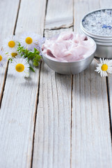 Fototapeta na wymiar pink moisturizer cream, blue bath salt and white flowers on natural rusty wood table
