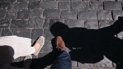 Top view of male and female legs walking along the sidewalk together. Sunny day