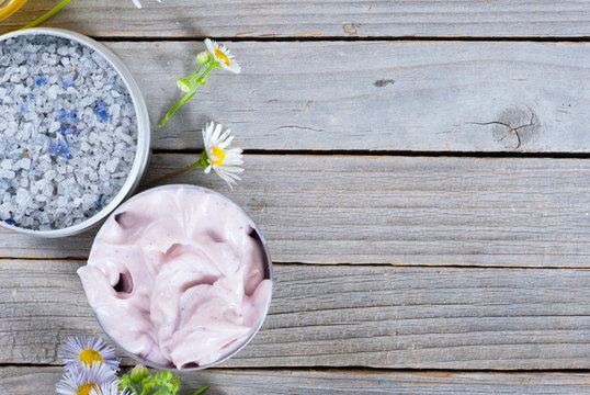 Pink Moisturizer Cream, Blue Bath Salt And White Flowers On Natural Rusty Wood Table