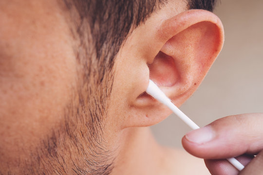 Man about to clean his ears using Q-tip cotton swab. Hygiene essentials concept. Removing wax from ear.