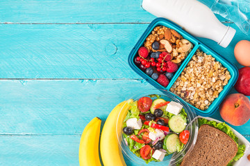 set of healthy lunch boxes with greek salad, sandwich, granola, vegetables, nuts, berries, banana, eggs, peaches and yogurt