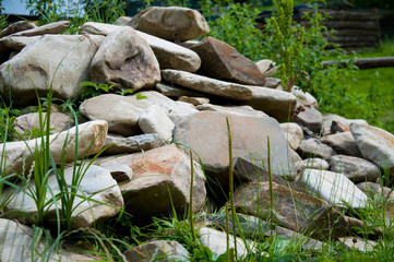 Green grass grows near a large pile of stones. Summer