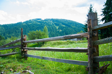 Old wooden fence in the mountains. Forest and tall trees. Mountains and hills. Summer