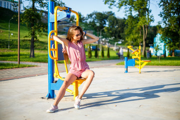 Young pretty sporty caucasian girl in a pink jumpsuit and sunglasses on the street sports field in the park on a sunny day in summer. Fitness on street sports ground.