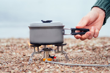 The pan with the porridge stands on the gas burner (Camping Stove). On the background of the river