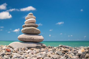 Fototapeta na wymiar Pebble pyramid on the beach on a background of blue sky with clouds on a sunny day. The concept of harmony of balance and meditation. copy space
