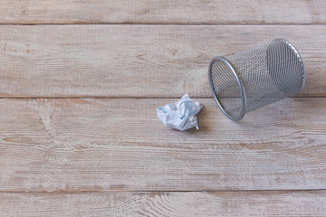 Crumpled sheet of paper and metal basket. On a wooden background.