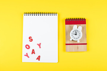 Back to school mockup concept. School time minimal concept. Notepad, pencil, alarm clock and red wooden letters on yellow background. Flat lay, top view, copy space
