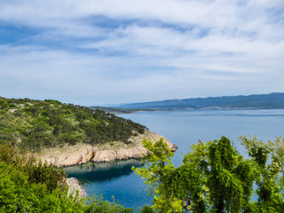 Fototapeta premium A sneak peak on a coastal line of Croatia from a hill. Steep slopes going down straight to the water. Hills are covered with lush green plants.At the bottom, the slopes are barren. Overcast.