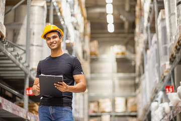 Smart Indian engineer man worker wearing safety helmet doing stocktaking of product management in...