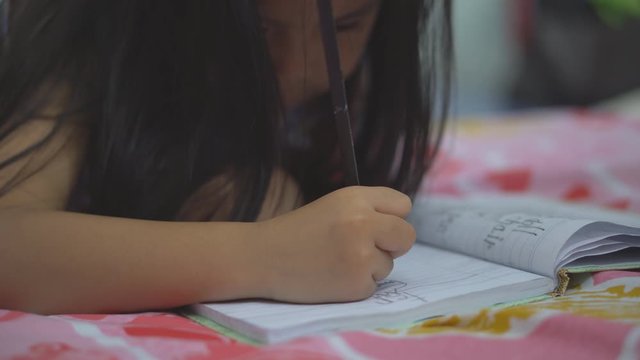 Asian child or kid holding pencil and student drawing and learning for write or paint on white paper for creative idea and art think at kindergarten classroom and nursery preschool or home on bed 4K