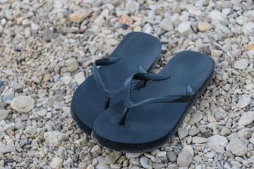 Black rubber flip-flops on pebbles, black flip flops on the beach, summer footwear example - Image