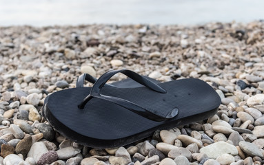 Black rubber flip-flops on pebbles, black flip flops on the beach, summer footwear example with the...