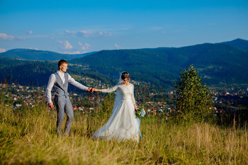 Newlyweds smile and hug each other among the meadow on top of the mountain. Wedding walk in the woods in the mountains, the gentle emotions of the couple, photo for Valentine's Day