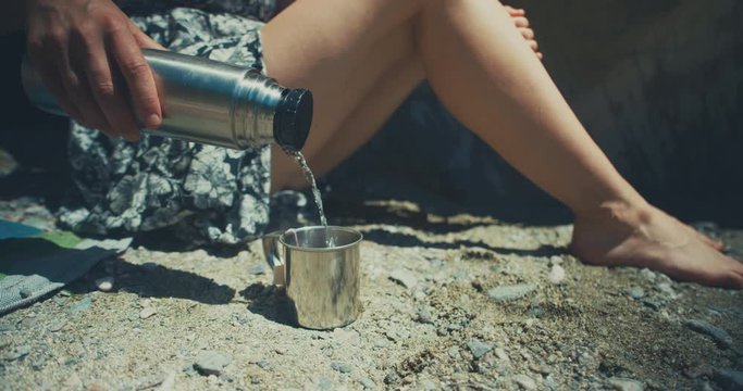 Young woman on beach pouring hot water from flask