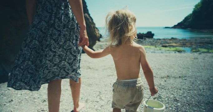 Young mother walking on beach with toddler holding a bucket