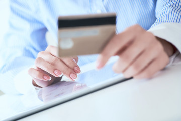 Close-up woman's hands holding a credit card and using tablet pc for online shopping. Middle section of young businesswoman making online payments with credit card and tablet.
