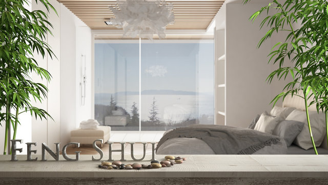 Wooden vintage table shelf with pebble and 3d letters making the word feng shui over blurred minimalist bedroom with double bed,shower and panoramic window, zen concept interior design