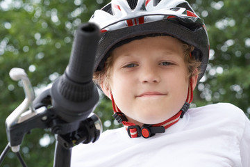 Small Caucasian boy cyclist in protective helmet put his head on the handlebar of the bike posing for the camera. a Boy rests during cycling in park on summer day. Weekend activity.