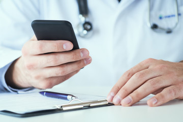 Male doctor hands with mobile phone close-up. Male doctor in white coat is using a modern smartphone device with touch screen.