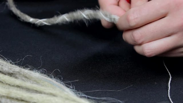 making artificial dreadlocks, female hands with colored nails with thread and a needle close-up, needlework and handmade